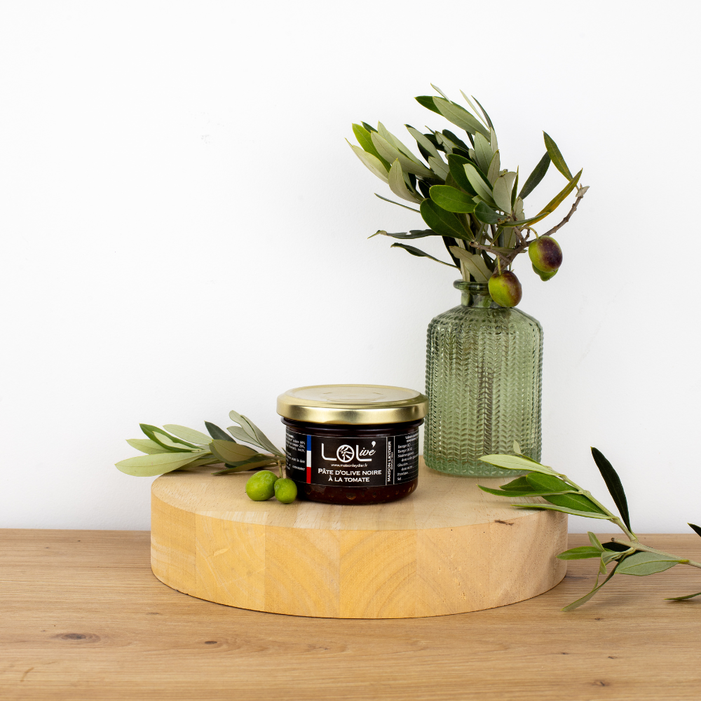 Pot de pâté d'olive noire à la tomate de Maison Leydier, sur fond naturel avec olives fraîches et branches d'olivier. Produit artisanal de qualité, fabriqué en France.