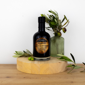 "Bouteille de vinaigre balsamique vieilli en fût de chêne de Maison Leydier, sur fond naturel avec olives fraîches et branches d'olivier. Produit artisanal de qualité, fabriqué en France.