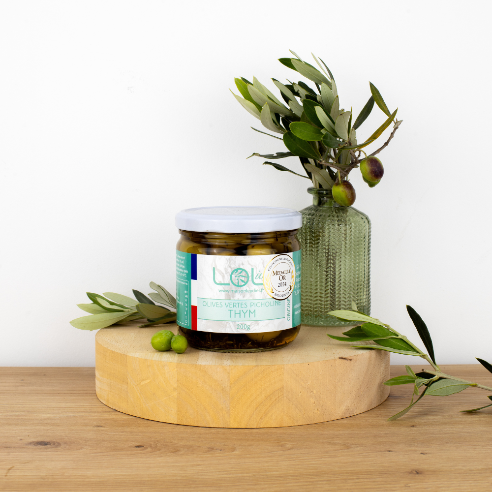 Pot d'olives vertes picholines au thym de Maison Leydier, sur fond naturel avec olives fraîches et branches d'olivier. Produit artisanal de qualité, fabriqué en France.
