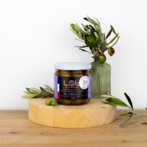 Pot d'olives vertes picholines à l'ail et au basilic de Maison Leydier, sur fond naturel avec olives fraîches et branches d'olivier. Produit artisanal de qualité, fabriqué en France.