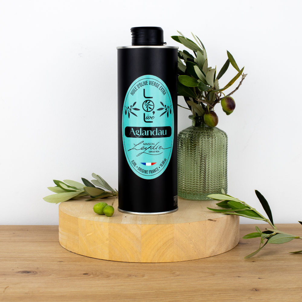 Bouteille d'huile d'olive vierge extra Aglan Dau de Maison Leydier, sur fond naturel avec olives fraîches et branches d'olivier. Produit artisanal de qualité, fabriqué en France.